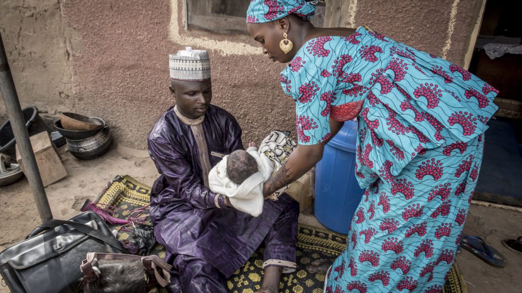 Barber Abdulaziz Lawn hands Abubakar Nafisatu to his mother, Nafisatu Bilyaminu, after shaving the newborn's head and asking his mother if he had been immunized.