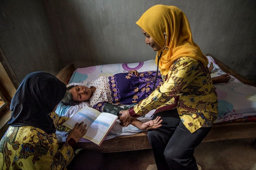 In Indonesia, a pregnant woman has her blood pressure taken while a nurse aid records data.